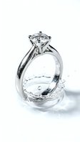 Sparkling diamond engagement ring with solitaire setting splashing into clear water creating ripples and bubbles on white background.