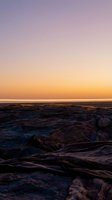 Serene coastal landscape at sunset with rocky shoreline, calm ocean waters, and gradient sky transitioning from purple to golden tones. Perfect for travel and nature projects.
