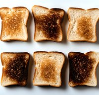 Slices of white bread toasted to different degrees from light golden to burnt brown arranged in two rows on white background, showing cooking progression.