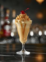 Creamy caramel milkshake with whipped cream and cherry garnish in elegant glass at upscale bar counter for dessert menu and beverage advertising.