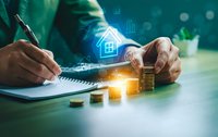 Businessman calculating mortgage loan with digital house icon and coin stacks on desk. Real estate investment planning and financial analysis concept.
