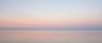 Serene dawn seascape with soft pastel colors reflecting on calm water, ideal for peaceful backgrounds and relaxation themes.