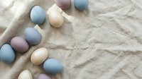 Pastel colored Easter eggs in soft blue, pink and cream tones arranged on natural linen fabric background for spring holiday celebration and festive decoration.