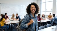 Happy African American female college student smiling in modern classroom with diverse classmates studying in background for education concepts.
