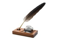 Feather quill pen with ink bottle on wooden base, isolated on white background for writing, calligraphy, and vintage desk decor design projects.