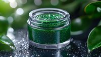 Sparkling emerald green cosmetic glitter in glass jar with scattered particles on dark surface against blurred background with green leaves and bokeh lights.
