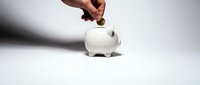 Hand inserting coin into white ceramic piggy bank on clean background for savings and financial planning concepts.