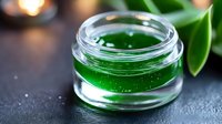 Bright green transparent gel or serum in glass jar on dark background with green leaves and bokeh lights, macro shot for cosmetic and skincare products.