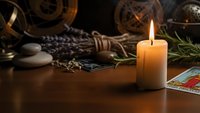 Mystical fortune telling setup with burning candle, tarot cards, crystals and herbs on wooden table for spiritual guidance and divination practices.