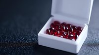Red gemstones displayed in white jewelry box on dark surface, showcasing precious rubies or garnets for luxury retail, engagement rings, and fine jewelry design projects.