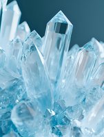 Cluster of clear blue quartz crystals with sharp faceted points, glowing with icy translucent light against a soft blue background.