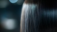 Silky smooth black hair close-up with soft bokeh background showing healthy, straight, shiny strands in macro photography style. Professional haircare and beauty concept.