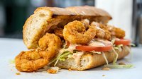 Crispy fried shrimp po boy sandwich with lettuce tomato onion on crusty bread roll served with golden onion rings on white surface ready for menu design.