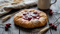 Rustic homemade pastry with red berry jam filling on wooden table with wheat stalks and coffee mug creating cozy breakfast scene for food photography.