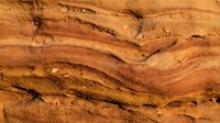 Layered sandstone rock texture with warm orange and brown tones, showing natural sedimentary patterns and geological formations as background.