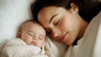 Young Asian mother and sleeping baby share tender moment on white bedding, faces close together in peaceful intimate bonding scene. Natural lighting enhances warm mood.