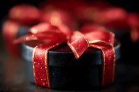Elegant black gift box wrapped with shimmering red satin ribbon and golden sparkles on dark background, creating luxurious holiday atmosphere.