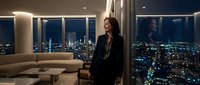 Woman in dark blazer standing in modern high-rise apartment with panoramic city night views, luxury interior design, urban lifestyle and contemporary living space.