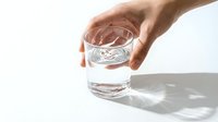 Hand holding a clear glass of pure water on white background, with light refractions casting elegant shadows, symbolizing hydration and wellness.