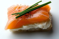 Fresh smoked salmon canape with cream cheese and chives on white bread, close-up view against light background, appetizer for catering and events.