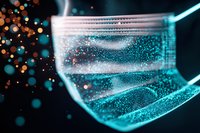 Macro view of surgical face mask with glowing turquoise particles and orange bokeh lights floating in dark background, healthcare protection concept.