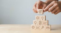 Business strategy concept with hands placing wooden blocks featuring target, gears, lightbulb and growth icons on desk for planning and development.