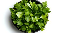 Fresh green parsley leaves in black bowl on white background, top view. Aromatic culinary herb isolated for food photography and cooking design.