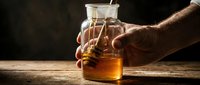 Male hand reaching for glass pitcher of golden honey on wooden surface with dark background, suitable for food, culinary, and wellness content.