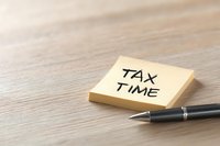 Tax time reminder written on yellow sticky note with pen on wooden desk surface, soft focus background for financial and accounting concepts.