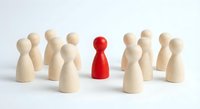 Red wooden pawn figure standing out among group of natural wood pawns on white background. Leadership and uniqueness concept for business presentations.