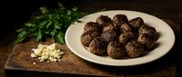 Homemade meatballs on white plate with fresh herbs and garlic on rustic wooden table for cooking and dining concepts.