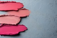 Smeared pink and coral lipstick or cream blush texture samples on gray concrete background. Cosmetic product swatches showing different shades of rose.