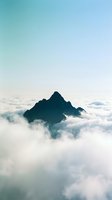 Dramatic mountain peak rising above dense cloud layer with serene turquoise sky, capturing aerial landscape for travel, nature, and inspirational design projects.