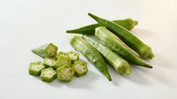 Fresh green okra pods with sliced cross-sections showing seeds on white background. Healthy organic vegetable ingredient for cooking and nutrition.