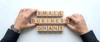 Businessman hands arranging wooden blocks spelling Small Business Grant on white background, symbolizing funding, entrepreneurship and financial support.