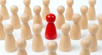 Red wooden pawn figure standing out among natural wood pawns on white background. Leadership, uniqueness and individuality concept for business presentations.
