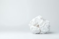 Crumpled white paper ball on light gray background with copy space, minimalist composition showing texture and shadows for creative design projects.