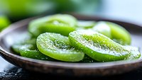 Fresh sliced green kiwi fruit arranged on dark ceramic plate with water drops, macro shot showing juicy texture and seeds. Natural food photography.