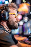 Caucasian male gamer with beard and glasses wearing headphones focused on competitive gaming, side profile against blurred colorful background with bokeh lights.