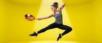 Young athletic woman jumping with frying pan in dynamic cooking pose against bright yellow background for culinary fitness lifestyle concepts.