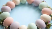 Pastel colored Easter eggs arranged in circular wreath formation with moss decoration on light blue background for spring holiday celebration.