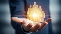 Businessman holding glowing team of people icons in cupped hands representing leadership, human resources management and corporate teamwork concepts.
