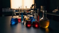 Laboratory glassware with colorful chemical solutions on dark table in research facility for scientific experiments and analysis work.
