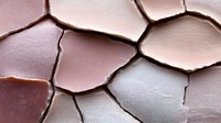 Cracked dry earth texture in pink and brown tones showing natural drought patterns and deep fissures. Abstract background for environmental concepts.
