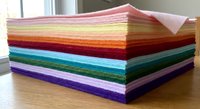 Colorful rainbow felt fabric sheets stacked in neat pile for crafting and sewing projects. Vibrant textile materials arranged by color gradient on wooden surface.