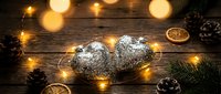 Traditional Christmas stollen cake with powdered sugar on rustic wooden table surrounded by warm fairy lights, dried orange slices and pine cones for holiday baking.