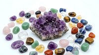 Large amethyst crystal cluster surrounded by colorful tumbled gemstones including quartz, jasper, and aventurine on white background for healing.