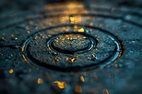 Macro photography of water drop impact creating concentric ripples with golden light reflections and scattered droplets on dark aqua surface. Artistic nature detail.