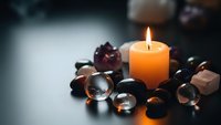 Burning orange candle surrounded by colorful gemstones and crystals creating peaceful meditation atmosphere for wellness and spiritual practices.