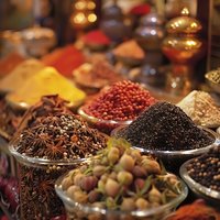 Aromatic spices and seasonings in traditional bowls at eastern market stall, including star anise, black pepper, pink peppercorns and dried herbs for cooking.